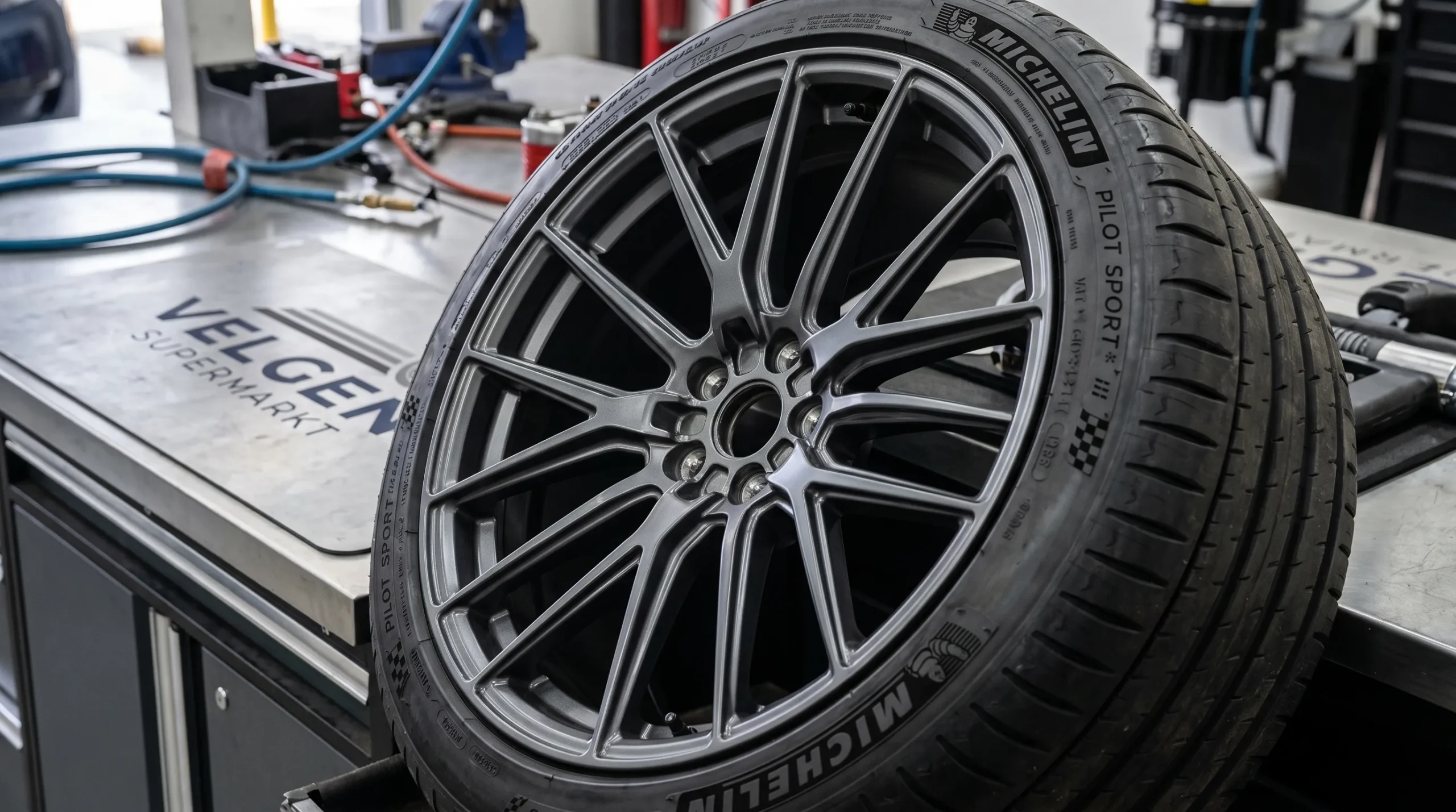 Close-up van een Tesla Model Y-velg naast een gemonteerde band, met focus op velgbreedte, naafgat en bandenprofiel in de werkplaats.