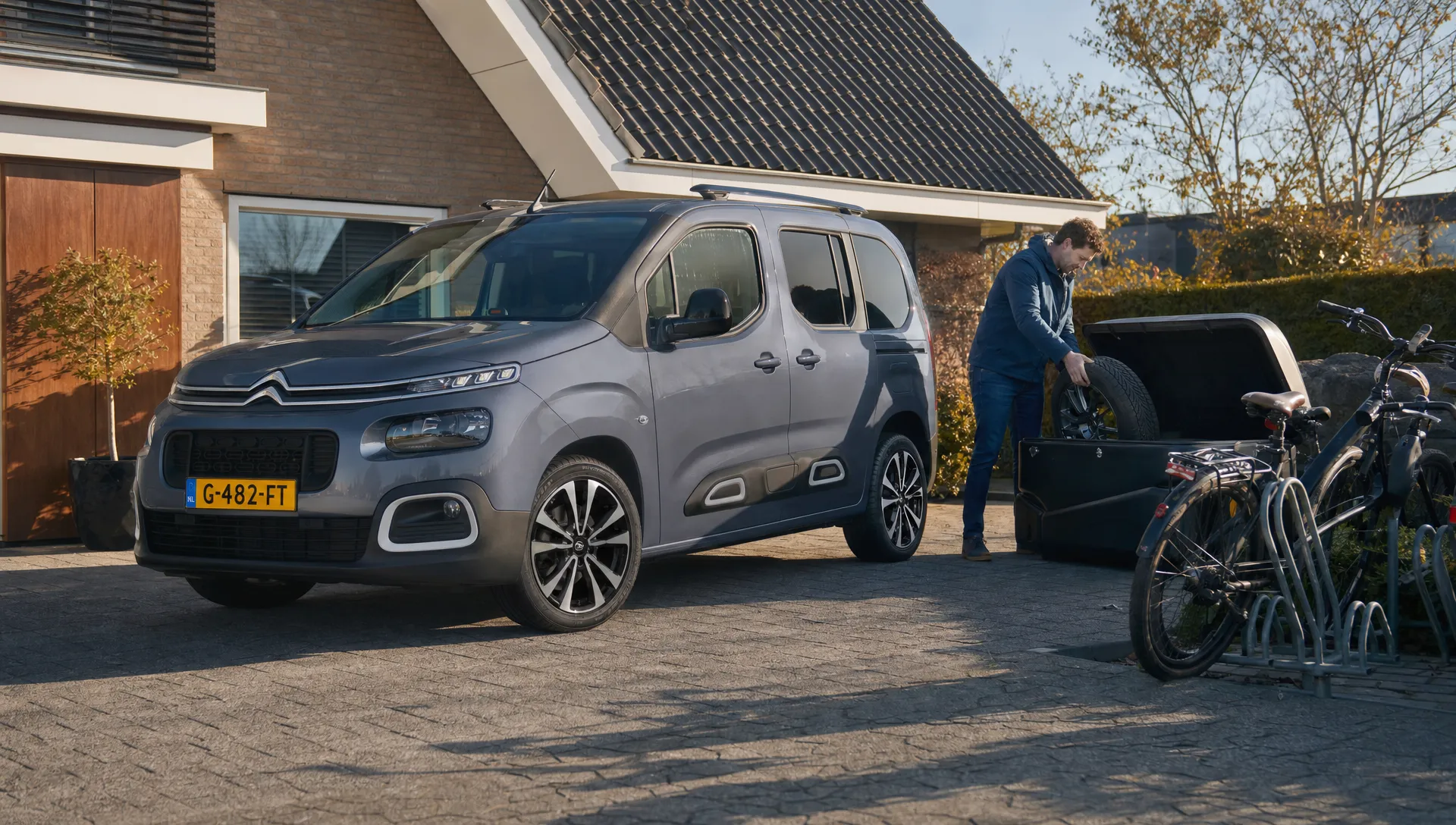 Een Citroën Berlingo met aluminium velgen staat geparkeerd naast een opbergbox voor seizoenswielen.