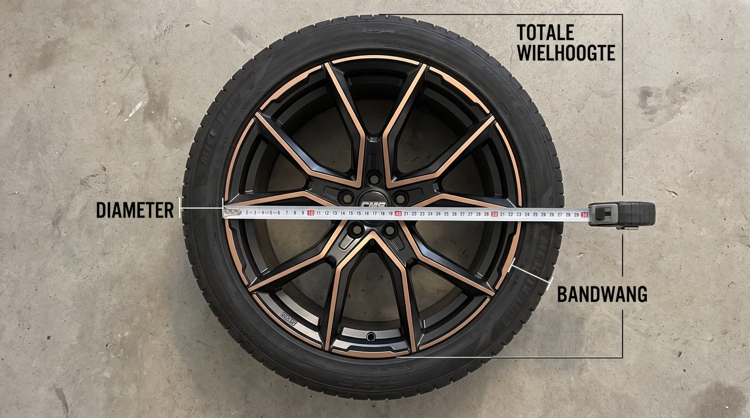 Een lichtmetalen velg met band naast een meetlint laat diameter, bandwang en totale wielhoogte zien.