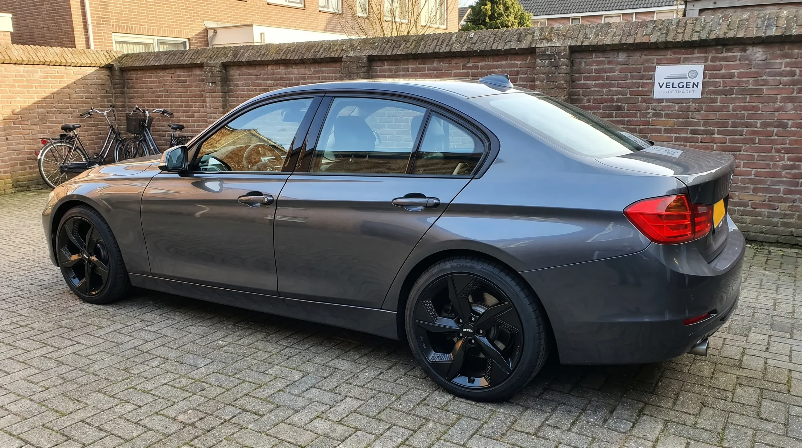 Een personenauto met DEZENT 18-inch velgen staat op een binnenplaats, met de bandwang en vrije ruimte in de wielkast zichtbaar.