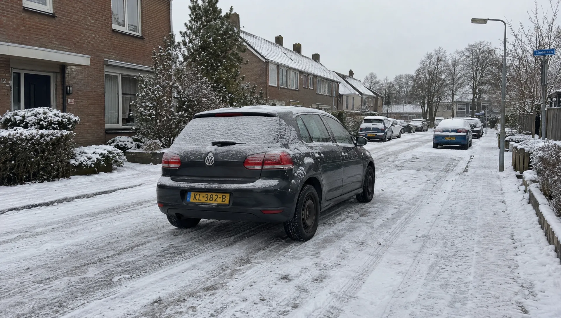 Een personenauto met stalen velgen en winterbanden staat geparkeerd in een besneeuwde woonstraat.