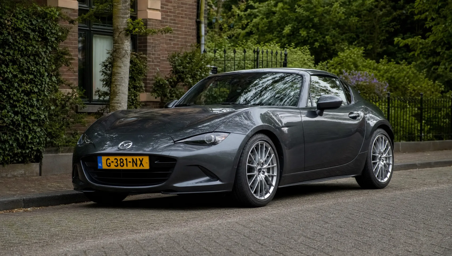 Een sportieve auto staat schuin geparkeerd op een rustige straat met multispoke lichtmetalen velgen die netjes binnen de wielkasten vallen.