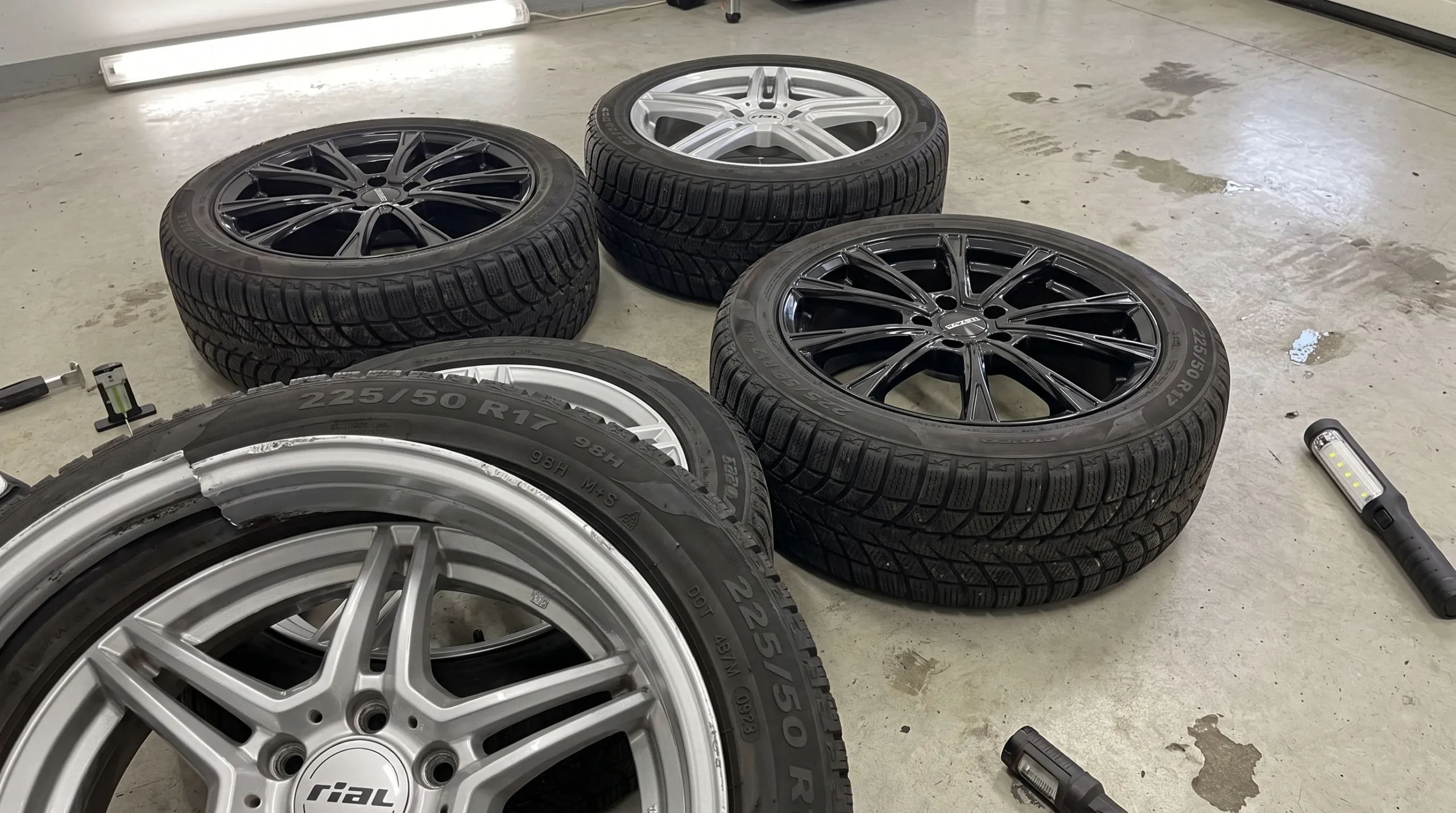 Vier winterwielen liggen op een schone garagevloer met aandacht voor profiel, velgrand, boutgaten, maat en DOT-code tijdens een inspectie.